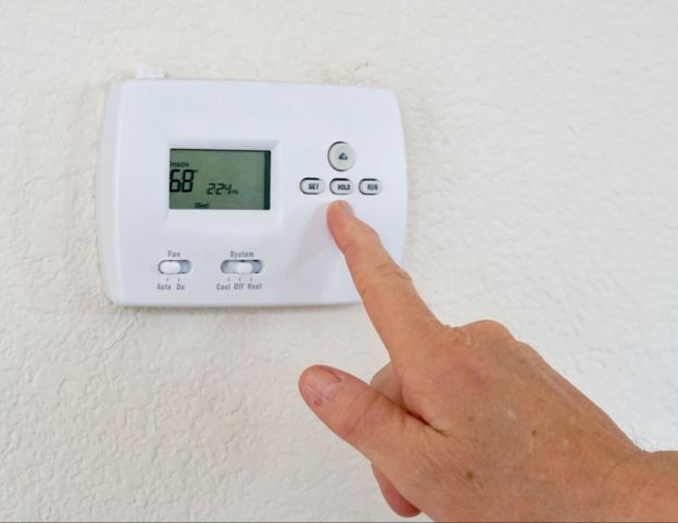 Person adjusting Thermostat on Wall 