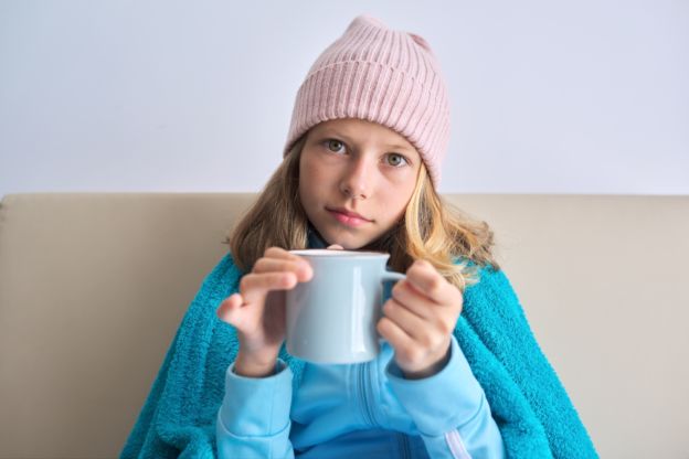 Little girl holding coffee mug bundled up on couch 