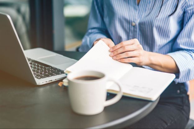 Woman working with laptop, notebook, and cup of coffee on table 